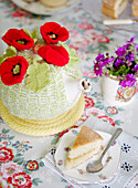 Tea cosy and slice of Victoria sponge cake on floral tablecloth