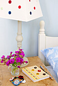 Notebook and bracelet with cut flowers and buttoned lampshade on wooden bedside table