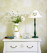 Cut flowers and lamp with flower motif on bedside cabinet