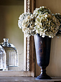Dried hydrangea in vase with mirror reflecting glass tableware in country home