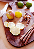 Cinnamon sticks and sliced lemon on chopping board with apple and chili peppers