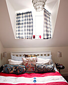 Checked blue and white curtains above bed with pink striped cover and an assortment of cushions