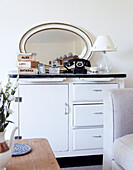 Rotary dial telephone and oval shaped mirror on white side unit