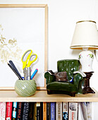 Ceramic armchair and ball of string on bookcase with artwork and lamp