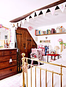 Wooden chest of drawers and brass footboard in girls attic bedroom