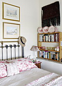Geblümte Kissen und Kopfteil aus Messing mit Bücherregal in einem Schlafzimmer im Landhausstil in Hexham, Northumberland, England UK