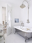 Freestanding metallic rolltop bath with silver shower fitting and trolley in London home UK