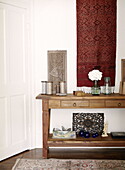 Vintage objects and red textile wall hanging above wooden console table in London townhouse UK
