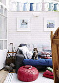 Katze sitzt auf abgenutztem Sofa mit gefalteten Decken in Wohnzimmererweiterung eines Londoner Hauses UK