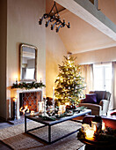 Spiegel über einem beleuchteten Kamin im Wohnzimmer mit beleuchtetem Weihnachtsbaum in einem festlichen Haus in Oxfordshire, England, UK
