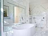 Large mirror above freestanding bath in marble bathroom of luxury London home, England, UK