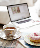 Heißer Tee und ein eisgekühlter Ring Donut mit einem Laptop im Hintergrund in einem Haus in Hastings, East Sussex, Großbritannien
