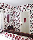 Oval shaped mirror with floral patterned wallpaper in bedroom with checked blanket, Oxfordshire home, England, UK