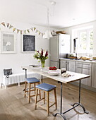 Blue retro bar stools at kitchen table with cut flowers and bunting in contemporary Oxfordshire cottage, England, UK