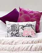 Pink and a purple cushion in contemporary bedroom of Oxfordshire cottage, England, UK