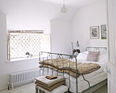 Metal framed bed in room with leaded window, Oxfordshire cottage, England, UK