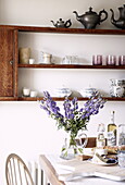 Cut flowers on dining room table with wall mounted shelving, Woodstock home, Oxfordshire, England, UK