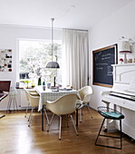 Retro chairs around table at window with blackboard and piano in Bussum home, Netherlands