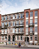 Frau radelt an einem Wohnhaus aus Backstein in Amsterdam, Niederlande, vorbei