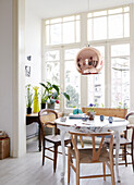 Variety of chairs at table under bronze metallic pendant light in contemporary apartment, Amsterdam, Netherlands