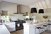 Open plan kitchen with black pendant lamps and stainless steel range oven and extractor, Oxfordshire, England, UK