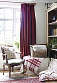 Korb und Stuhl mit Bücherregal am Fenster mit karierter Decke, Oxfordshire, England, UK
