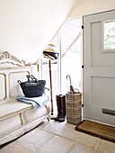 Hat stand with boots and a basket on gilded bench seat at front door in Oxfordshire, England, UK