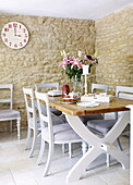 Kitchen table and chairs with clock in exposed stone dining room of barn conversion in Oxfordshire, England, UK