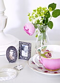 Framed photographs and cut flowers with pink teacup and engagement ring in Oxfordshire home, England, UK