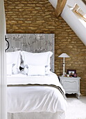 Doppelbett im Dachgeschoss eines umgebauten Hauses mit freiliegender Steinmauer, Oxfordshire, England, UK