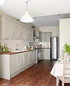 Fitted kitchen with wooden flooring and upright fridge in North London home, England, UK