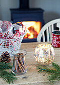 Beleuchtete Kerze mit Zimtstangen und Weihnachtskugeln auf dem Tisch in einem Haus in Devonshire, UK