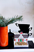 Kiefernnadeln in orangefarbener Vase mit ausgeschnittenen Teetassen und Modellhaus in London home England UK