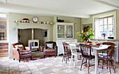 Pair of brown leather armchairs and woodburning stove with dining table and chairs in Oxfordshire farmhouse England UK