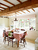Wooden chairs with red and white tablecloth in beamed Surrey farmhouse kitchen England UK