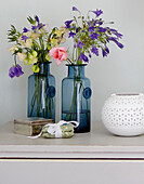 Cut flowers in blue glass vases with candle holder in bedroom of Surrey farmhouse England UK
