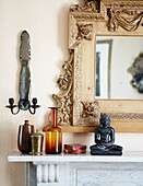 Vintage glassware and buddha statue with carved mirror frame on mantlepiece in London townhouse England UK