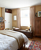 Beige blanket on white double bed with carved wooden furniture in London townhouse England UK