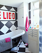 Freistehende Badewanne mit schachbrettartiger Wand und Badezimmerschrank in einem Einfamilienhaus in Margate, Kent, England