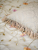 Fringed cushion on embroidered bed cover in traditional country house Welsh borders UK
