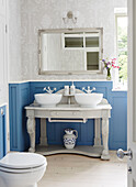 Double basins on wash stand in blue panelled bathroom of rural Oxfordshire cottage England UK