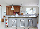 Chrome barstools at grey breakfast bar with wooden cupboard in UK kitchen