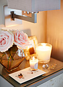 Lit candles and pink roses on side table in UK home