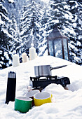 Saucepan on gas hob with flask and cups in snow, St Anton, Tyrol, Austria