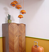 Orange suitcase and pendant lights with vintage wardrobe in Notting Hill home West London UK
