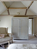 Light grey wardrobe and sofa in beamed Buckinghamshire bedroom UK