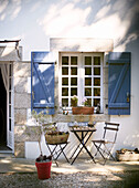 Klappstühle und Tisch unter dem Fenster mit blauen Fensterläden auf der Terrasse eines bretonischen Bauernhauses in Frankreich
