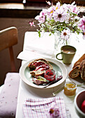 Marmelade und Brot mit Schnittblumen auf dem Frühstückstisch in einem bretonischen Landhaus in Frankreich