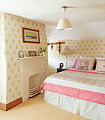 Quilt on double bed at fireside with floral wallpaper Devonshire cottage UK