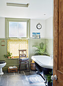 Hellgrün getäfeltes Badezimmer mit Vintage-Stuhl und Roll-Top-Badewanne in einem Haus in Kent England UK